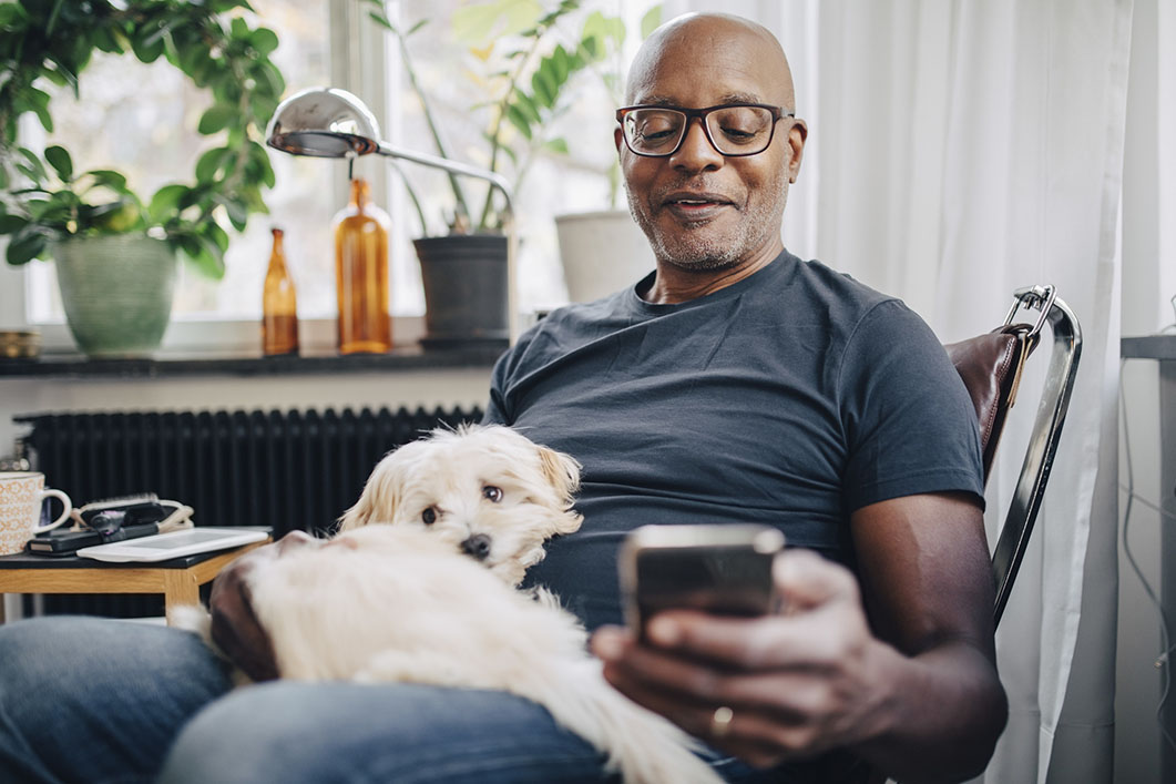 Man sitting with dog, using smartphone