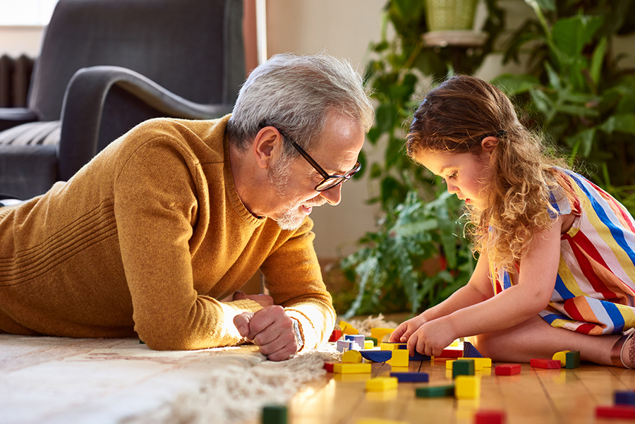 Young girl playing with wooden blocks and grandfather watching