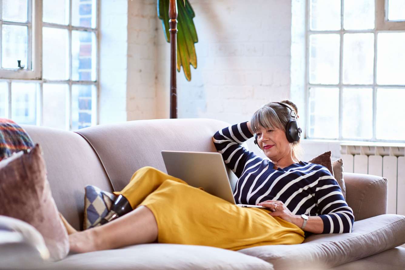 Middle-aged lady on the sofa listening to music on her laptop