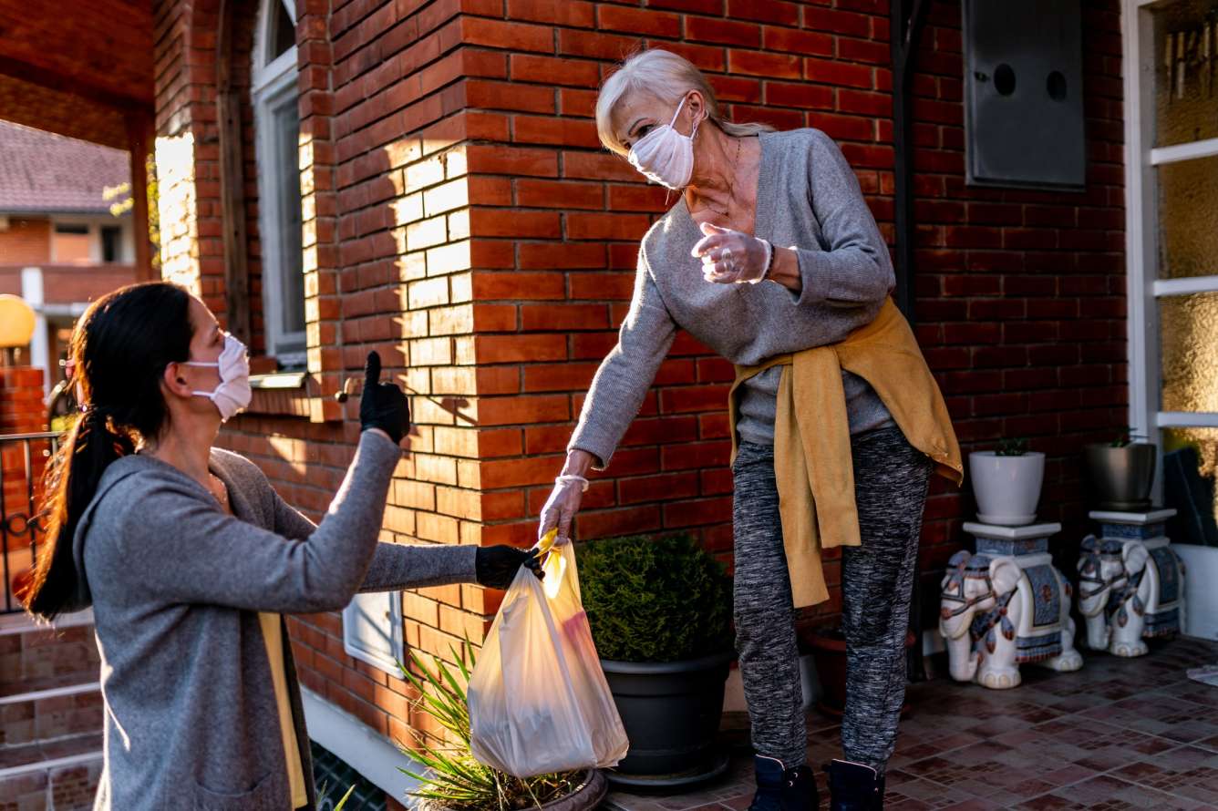 Female volunteer bringing groceries to an elderly woman at home