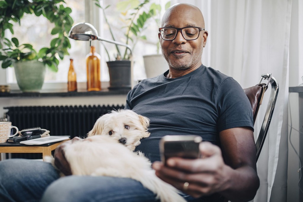 Man sitting with dog, using smartphone