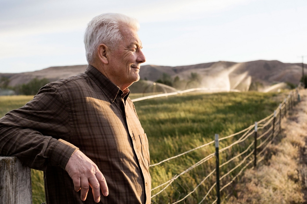 Older man leaning against a fence